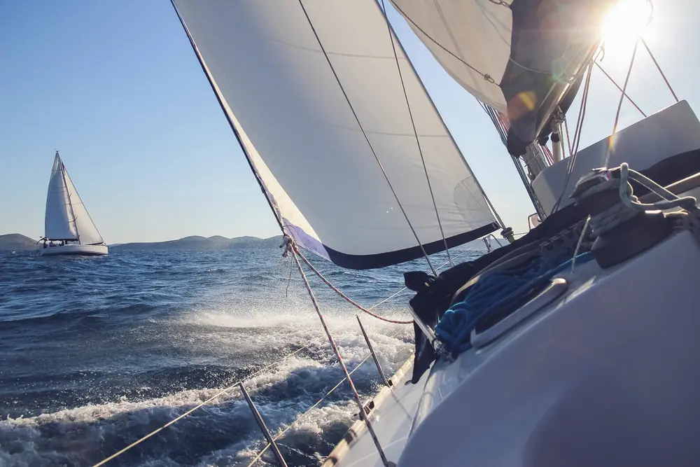 White yacht sails filled with wind above sparkling sea water