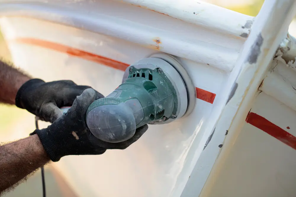 Gloved worker sanding or polishing the white side of a boat