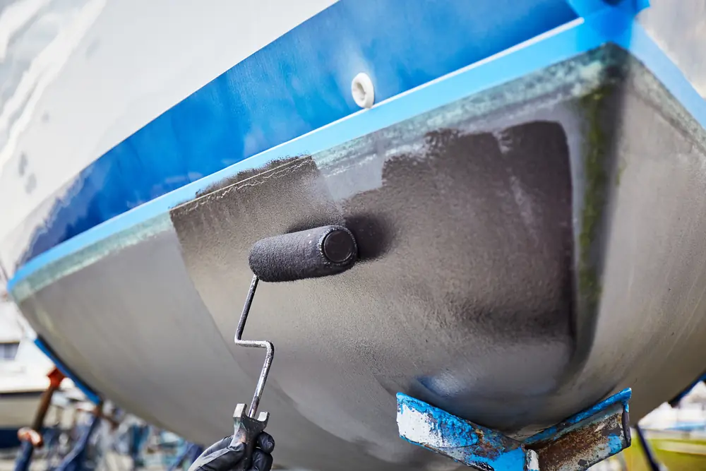 Roller applying dark antifouling coating to the lower hull of a yacht